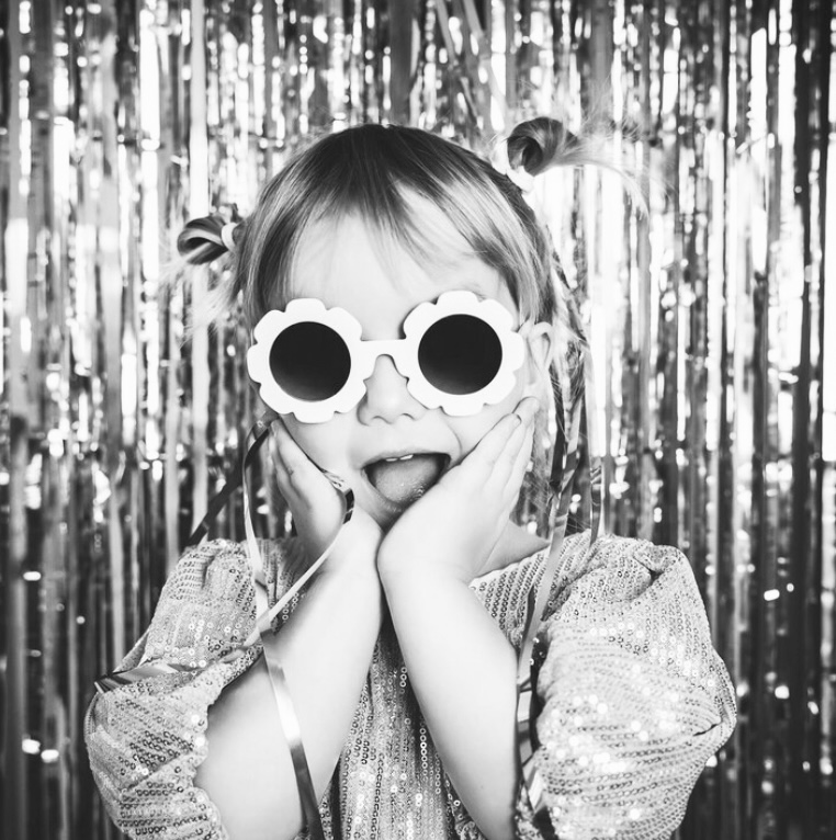 Adorable child with flower sunglasses and metallic backdrop